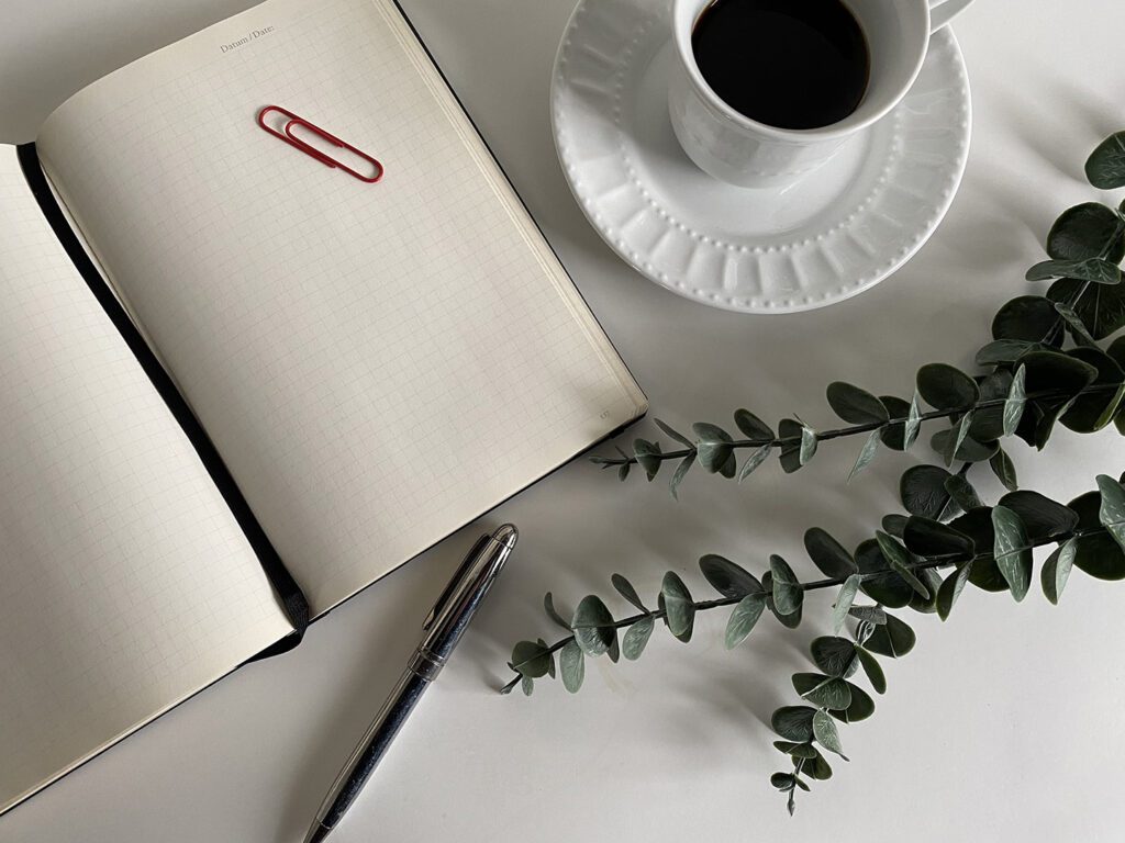 looking down to a notepad and pen with a coffee on a white table